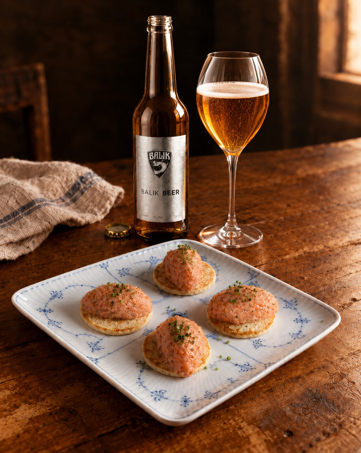 BALIK Beer im Weinglas mit Flasche und Blinis mit Lachstartar auf Holztisch (Bild mit KI erstellt)