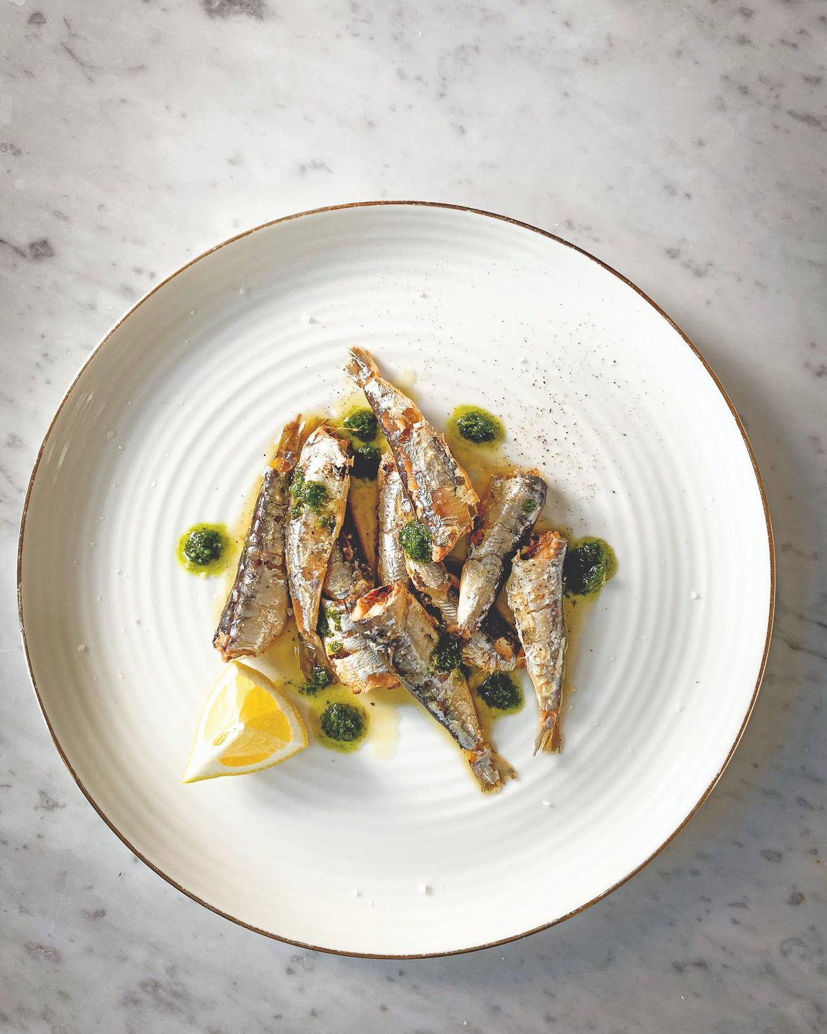 Kleine Fische mit Kräutersauce und Zitrone auf einem weissen Teller